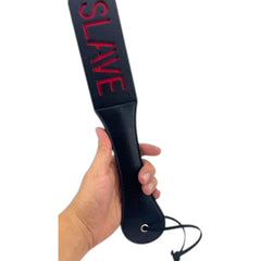 Paleta de azotes negra de cuero sintético con la palabra SLAVE grabada en rojo. Glow&Vibe.