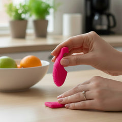Dedal vibrador fucsia de silicón Silk Finger de Glow&Vibe sostenido por una mano sobre una mesa de madera